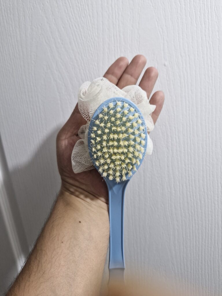 Demonstration of the double-headed bath brush while in use, emphasizing usability issues related to its flimsy design and small brush area.